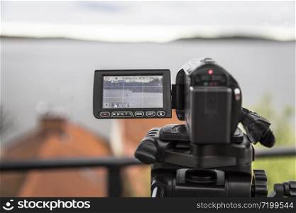 A video camera mounted on a tripod shoots a landscape with a yacht