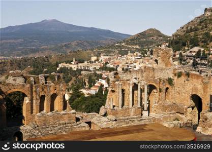 A view from high up in the cheap seats in the ancient Roman theatre or Teatro Antico of Taormino in Sicily shows the city and then the cone of the Mt. Etna volcano in the distance.