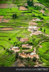A view from high up of some houses and green agricultural land, set against slope in the rural area of the Kabale district in Southern Uganda.