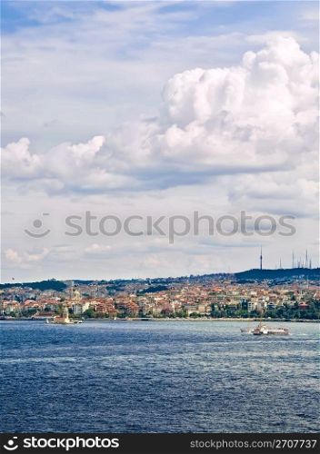 A view from Topkapi Palace, towards a famous landmark,The Maiden Tower, and a ferry boat passing by on a cloudy day.