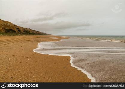 A view of a beautiful long and empty beach with shore break and high sand dunes behind