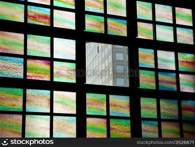 A view of an office building through one clear window surrounded by colored glass panes.