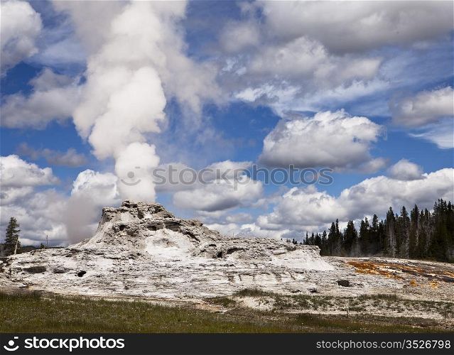 A view of Castle Geyser in Upper Geyser Basin showing steam rising from the vent in the central cone which has formed over years of steady eruptions. This is one of the larger volcanic geysers in Yellowstone National Park.