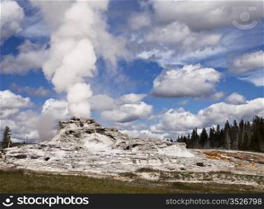 A view of Castle Geyser in Upper Geyser Basin showing steam rising from the vent in the central cone which has formed over years of steady eruptions. This is one of the larger volcanic geysers in Yellowstone National Park.