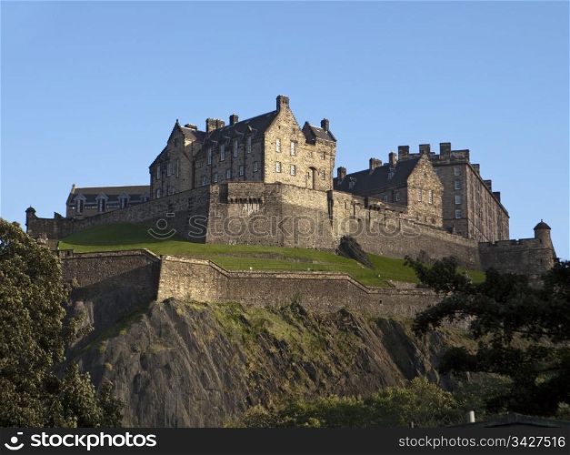 A view of Edinburgh Castle from below showing the rocky cliffs, ramparts and other defenses from attack.