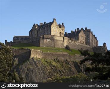 A view of Edinburgh Castle from below showing the rocky cliffs, ramparts and other defenses from attack.