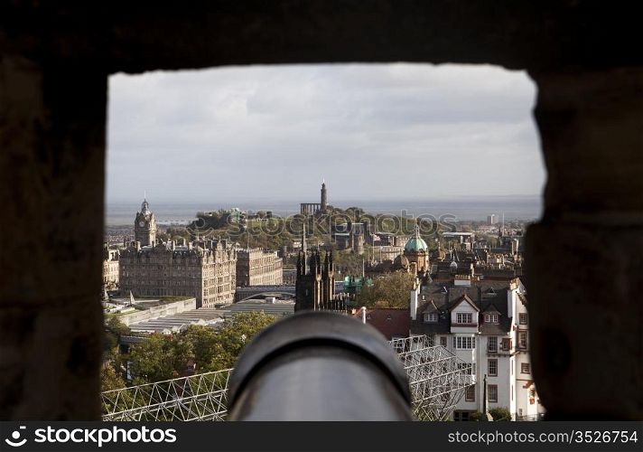 A view of Edinburgh framed through one of the rough stone gunports of Edinburgh Castle. The Old City is in the foreground and parts of the New City and Calton Hill are in the background.
