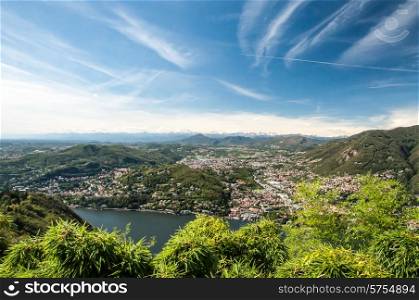 A view of Lake Como, the Town called Como and the Alps in the far distance with blue skys and white clouds.