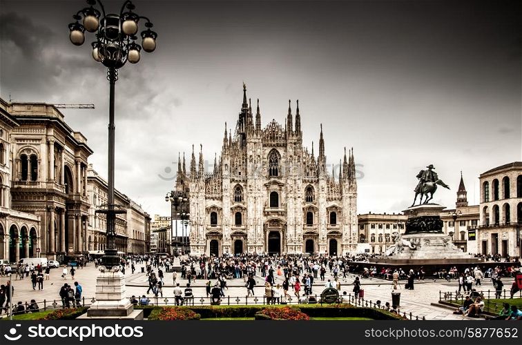 A view of Milan Cathedral fromthe front, including the large square filled with people in front of it, and some buildings to the side.