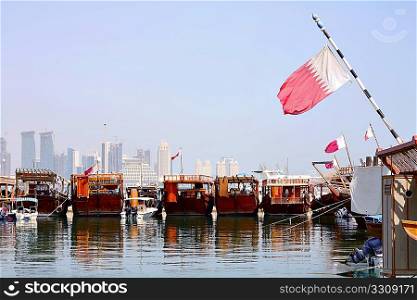 A view of the dhows in Doha harbour, with the Qatari flag flying from them and the new city skyline in the background.
