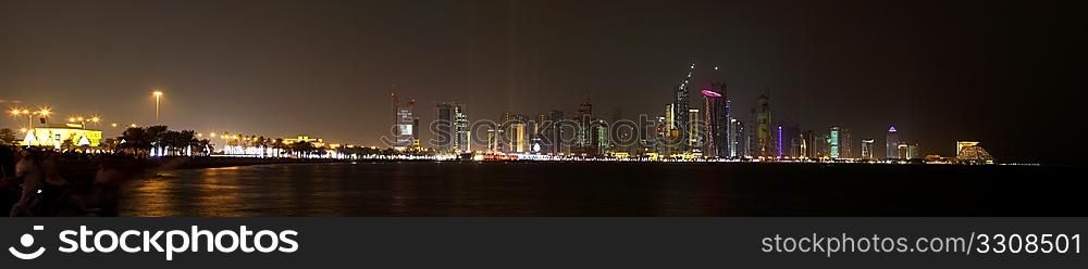 A view of the the skyline of Doha lit up for National Day, 2009, just ahead of the firework display, logos removed. Part of the crowd can be seen on the left, blurred by the long exposure.