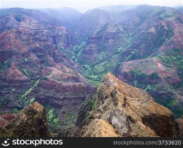 A view of the Waimea Canyon on the island of Kauai that highlights the volcanic red rocks with the bright green vegetation of the jungle.