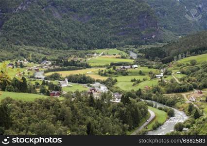 a village in norway with some houses and a church in the mountains near the river