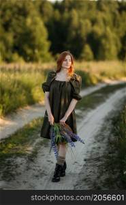 A village red-haired girl walks along a rural road in summer.. Portrait of a village girl on a rural road 3292.