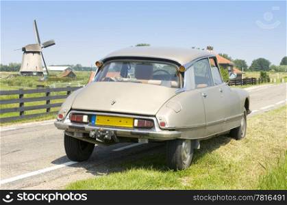 A vintage 1973 Citroen DS parked on a country road with a windmill in the distance on a bright summer day.
