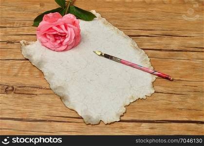 A vintage fountain pen with old paper and a pink rose