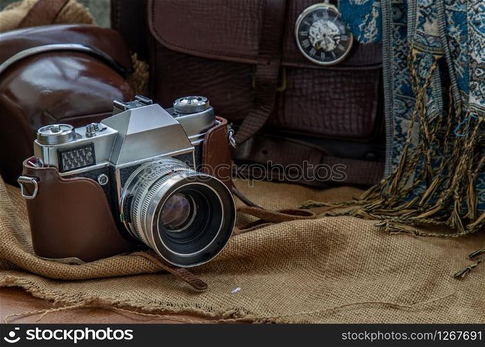 A vintage photo camera and A Brown leather bag with Scarf and Pocket watch on Sack cloth background. Holiday traveling concept design. Vintage color tone.