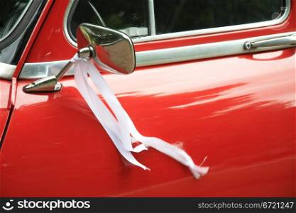A vintage red car had a white ribbon on its mirror as a wedding decoration
