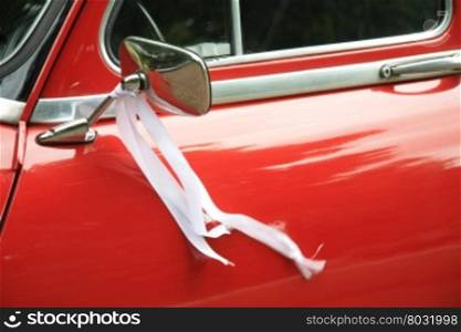 A vintage red car had a white ribbon on its mirror as a wedding decoration
