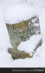 A vintage stone carved British road sign covered in winter snow and showing distances to London, Reading, Newbury and Bath