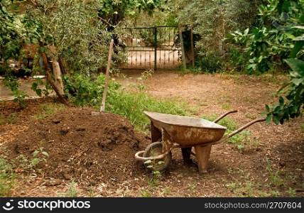A wagon/wheelbarrow next to manure hill and spade, under olive trees.
