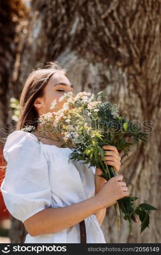 A walk of a joyful girl with a bouquet of daisies in a summer park.. A beautiful slender girl with a bouquet of wildflowers on the background