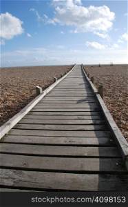 A walkway made of wooden slats stretching across the shingle beach at Dungeness in Kent, England