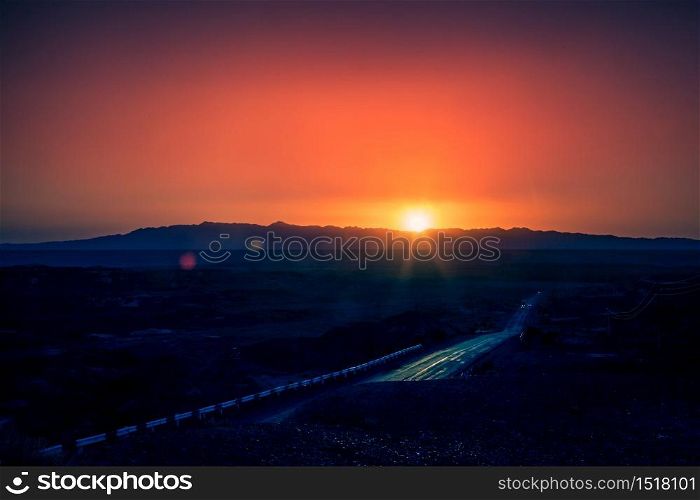 A warm sunset over the highway in a purple-orange color with mountains on the horizon