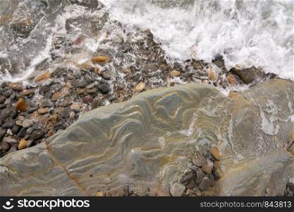 A wave rolls onto a rocky sea beach