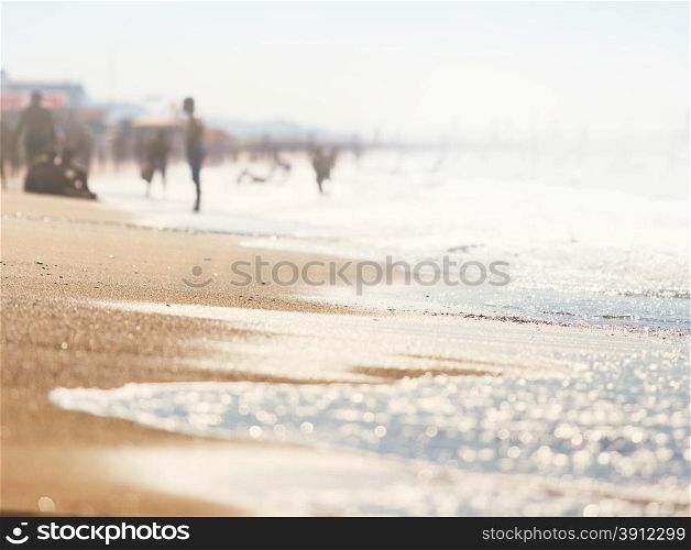 A wave thinning out of the sand of a beach, defocused people on the background