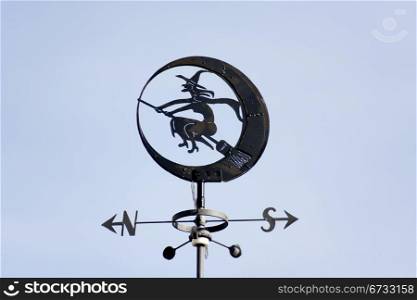 a weathervane with a witch sitting on the moon, on top of a house