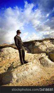 A well dressed man stands in an unusual landscape