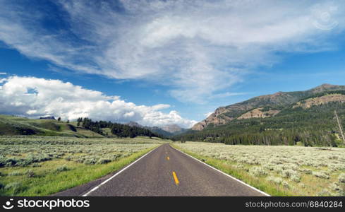 A well preserved two lane road leads to a vanishing point in the mountains