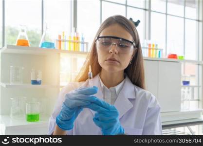 A western scientist woman holding an injection needle to analysis and develop vaccine of covid-19 virus in lab or laboratory in technology medical, chemistry, healthcare, research. Experiment science.