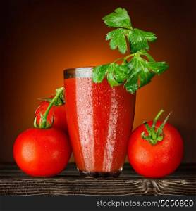 A wet glass of tomato juice decorated with parsley and ripe tomato bunch on a wooden table.