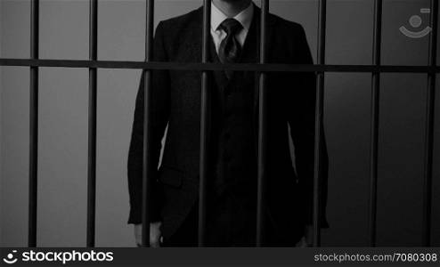 A white collar criminal stands behind bars in jail