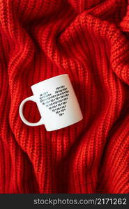 A white cup with a heart stands on a red knitted fabric. The concept of love and celebration of St. Valentine&rsquo;s day, February 14th. A white cup with a heart stands on a red knitted fabric. The concept of love and celebration of St. Valentine&rsquo;s day, February 14th.