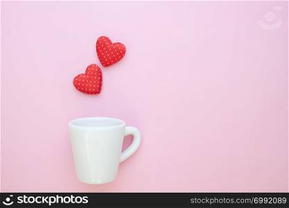 A white cup with polka dots red hearts on pink background. Copy space