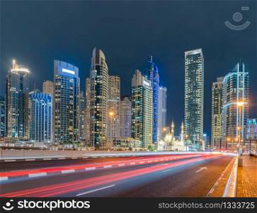 A white mosque near Dubai marina in downtown skyline, United Arab Emirates or UAE. Financial district and business area in smart urban city. Skyscraper and high-rise buildings at night.