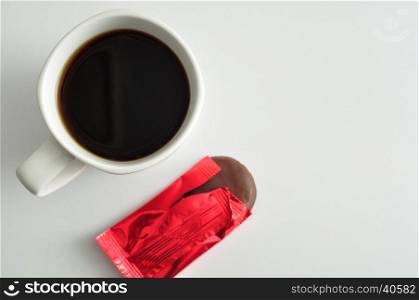 A white mug of coffee with a chocolate cover biscuit in a red wrapper