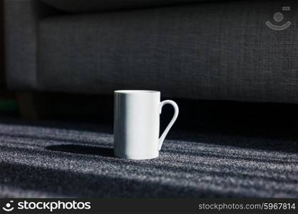A white mug on a carpet by a sofa at home