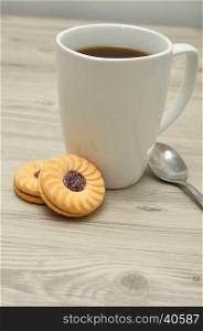 A white mug with coffee and round jam filled biscuits