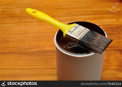 A white plastic container filled with brown paint and a yellow paintbrush