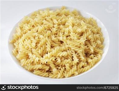 A White plate with uncooked raw fusilli spiral pasta.