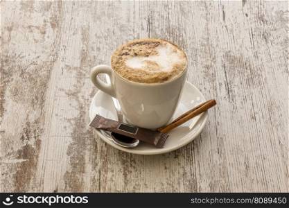 A white porcelain cup of coffee with a cinnamon stick and conventional sugar packet