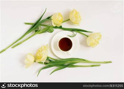 A white porcelain cup with black tea on a saucer surrounded by spring yellow tulips on a white background. The concept of spring, women’s and mother’s day, birthday or blogging