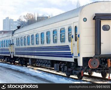 A white railroad car with blue stripes stands on the tracks on a bright sunny winter day.. The white railroad car of the train stands on the tracks on a bright winter day.