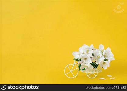 A white retro toy bicycle delivering white apple blossoms on a yellow background. Valentine&rsquo;s day card, birthday gift, Women&rsquo;s Day. Delivery of holiday goods. Spring concept with copy space