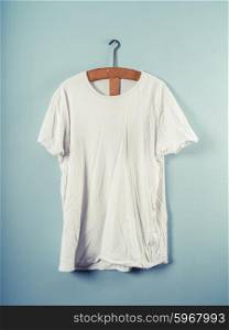 A white T-shirt hanging on a wooden hanger against a blue wall