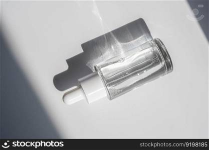 A white transparent bottle with serum in the rays of the sun. Laconic bottle shape.. A white transparent bottle with serum in the rays of the sun.